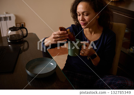 Woman Enjoying Pastry While Sipping Coffee at Home Office Desk with Laptop and Relaxed Morning 132785349