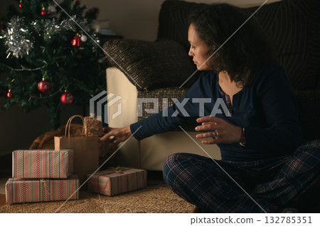 Woman Arranging Christmas Gifts Under Tree in Cozy Living Room During Holidays 132785351