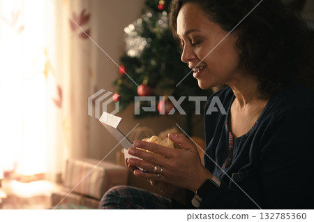 Woman Opens Gift Box By Christmas Tree In Cozy Home Holiday Moment Woman Opens Gift Box By Christmas Tree In Cozy Home Holiday Moment 132785360