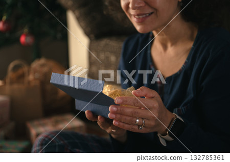 Woman Opens Blue Gift Box With Warm Smile During Cozy Holiday Moment At Home 132785361