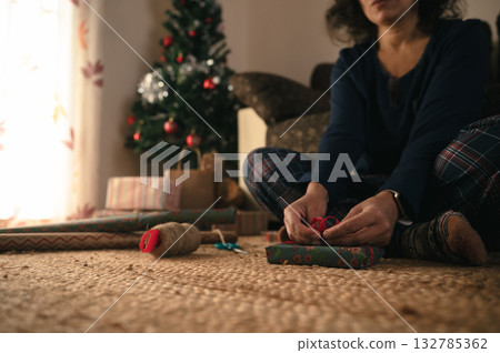 Person Wrapping Christmas Gifts on Floor Near Tree in Cozy Home Holiday Setting 132785362