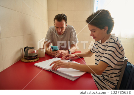 Father And Son Study At Red Table With Laptop And Notebook In Bright Kitchen 132785628
