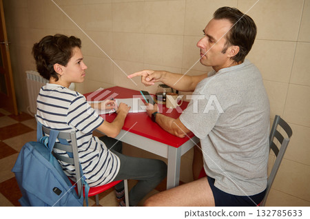 Man And Teen Discuss Homework At Kitchen Table In Casual Setting 132785633