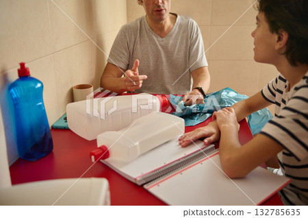 Two People Discussing At A Red Table With Large Bottles, Notebook, And Gloves Two People Discussing At A Red Table With Large Bottles, Notebook, And Gloves 132785635