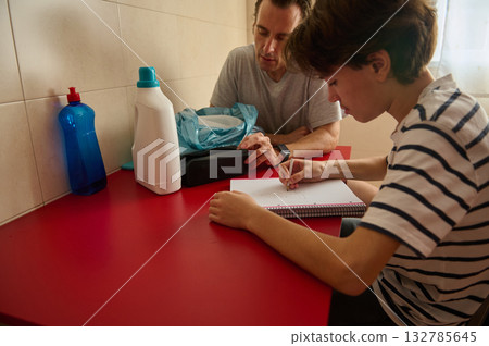 Father And Teen Study Session At Red Table With Notebook And Supplies Father And Teen Study Session At Red Table With Notebook And Supplies 132785645