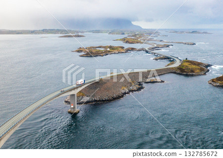 Truck driving across a curved section of the Atlantic Ocean Road connecting small coastal islands in Norway, surrounded by sea and rugged landscape 132785672