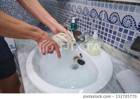 Person Washing Cloth Under Faucet in Bathroom Sink With Soap Dispenser and Mosaic Tile Background Person Washing Cloth Under Faucet in Bathroom Sink With Soap Dispenser and Mosaic Tile Background 132785770