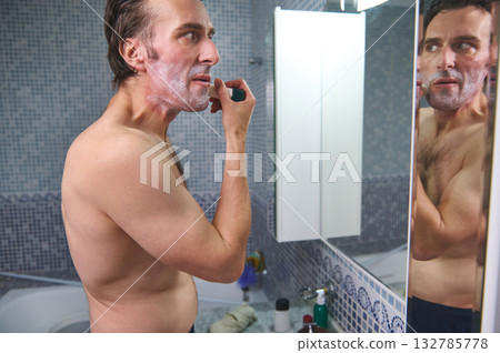 Man Shaving in Bathroom Mirror With Foam on Face, Grooming at Home 132785778