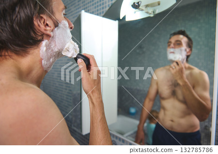 Man Shaving In Mirror With Foamy Beard While Child Watches In Background 132785786