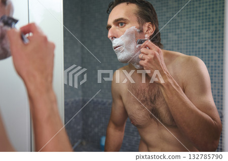 Man Shaving in Bathroom Mirror With Foam, Razor in Hand, Preparing for Day Man Shaving in Bathroom Mirror With Foam, Razor in Hand, Preparing for Day 132785790