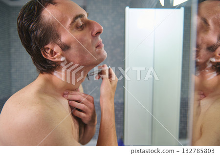 Man Shaving in Bathroom Mirror, Close-Up Grooming Moment During Morning Routine 132785803