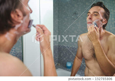 Man Shaving in Modern Bathroom Mirror With Razor and Foam, Reflecting Confidence Man Shaving in Modern Bathroom Mirror With Razor and Foam, Reflecting Confidence 132785806
