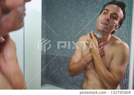 Man Shaving in Glass Shower Mirror With Foamy Cream and Razor 132785809