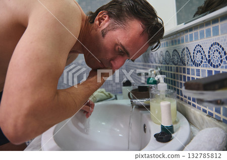 Man Washing Face At Sink In Bathroom With Soap Dispenser And Mirror Mosaic Tiles Man Washing Face At Sink In Bathroom With Soap Dispenser And Mirror Mosaic Tiles 132785812