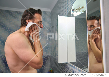 Man Shaving in Bathroom Mirror, Cleaning Face With Towel During Morning Grooming Man Shaving in Bathroom Mirror, Cleaning Face With Towel During Morning Grooming 132785823