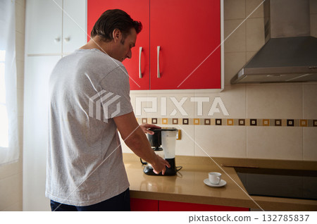 Man Brewing Coffee in Modern Kitchen With Red Cabinets and Coffee Maker Man Brewing Coffee in Modern Kitchen With Red Cabinets and Coffee Maker 132785837