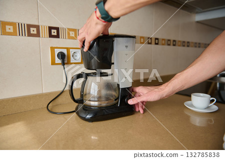 Hands Operating a Coffee Maker on Kitchen Counter with Coffee Cup Nearby Hands Operating a Coffee Maker on Kitchen Counter with Coffee Cup Nearby 132785838