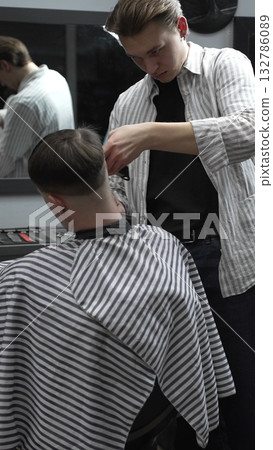 Professional barber carefully trimming customer's hair with electric clipper, providing a stylish and precise haircut in a modern barbershop environment Professional barber carefully trimming customer's hair with electric clipper, providing a stylish and precise haircut in a modern barbershop environment 132786089