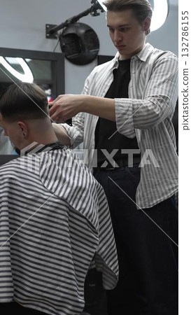 Professional barber carefully trimming customer's hair with electric clipper, providing a stylish and precise haircut in a modern barbershop environment 132786155