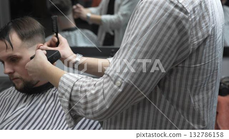 Professional barber cutting client's hair with electric clipper, working precisely in contemporary barbershop, delivering clean and sharp hairstyle 132786158