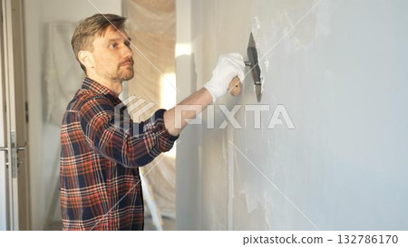 Male construction worker wearing protective gloves smoothing plaster onto wall surface during home renovation using professional trowel tool Male construction worker wearing protective gloves smoothing plaster onto wall surface during home renovation using professional trowel tool 132786170
