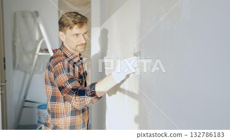 Male construction worker wearing protective gloves smoothing plaster onto wall surface during home renovation using professional trowel tool Male construction worker wearing protective gloves smoothing plaster onto wall surface during home renovation using professional trowel tool 132786183