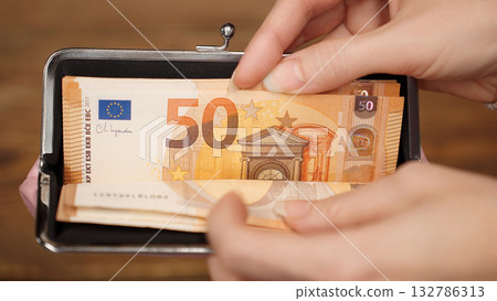 Woman's hands holding a wallet with 50 euro banknotes inside. Cash payment or savings concept for personal finance. Ideal for budgeting or financial education content. Woman's hands holding a wallet with 50 euro banknotes inside. Cash payment or savings concept for personal finance. Ideal for budgeting or financial education content. 132786313