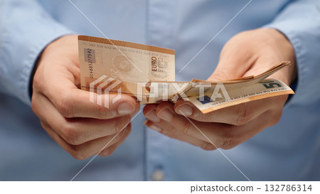 Close-up of male hands counting euro banknotes. Man in blue shirt holds European currency. Financial concept background for salary, savings or budget planning in EU. Close-up of male hands counting euro banknotes. Man in blue shirt holds European currency. Financial concept background for salary, savings or budget planning in EU. 132786314