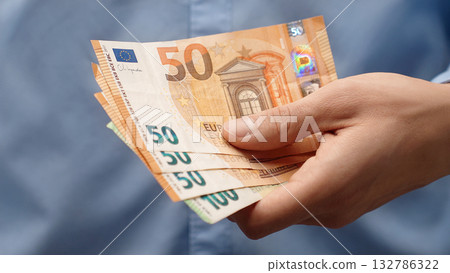 Close-up male hand holding euro banknotes. Financial concept for savings, future wealth, investment or personal finance. Ideal for educational content or financial background. Man holds euro bills Close-up male hand holding euro banknotes. Financial concept for savings, future wealth, investment or personal finance. Ideal for educational content or financial background. Man holds euro bills 132786322