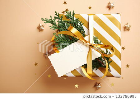 Christmas golden and white gift box with empty rectangular tag on beige background. Copy space 132786993
