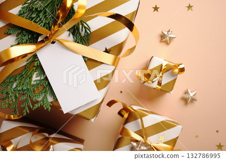 Close-up of white and gold striped gifts with blank label on beige background. Selective focus. Copy space. Close-up of white and gold striped gifts with blank label on beige background. Selective focus. Copy space. 132786995