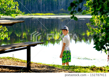 Teen boy at the little forest lake in hot summer day. 132787411