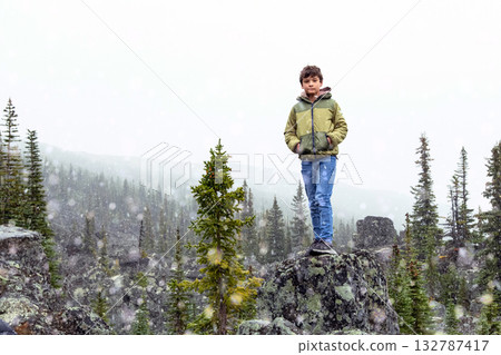 Boy stands among big rocks geological formation in the mountains. Boy stands among big rocks geological formation in the mountains. 132787417