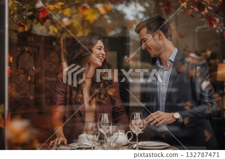 Autumn leaves swirl beyond rustic window as warm reflections reveal laughter and shared intimacy 132787471