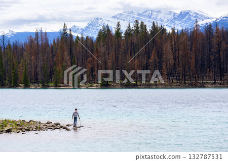 Teen hiker at the lake among mountain peaks and burnt forest. 132787531