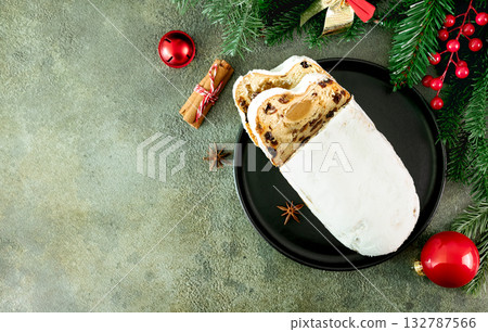 Christmas marzipan stollen decorated with fir branches and holiday ornaments on green background. Top view. Copy space. 132787566