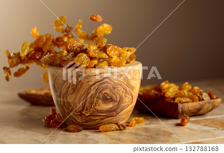 Yellow sultana raisins pour into a wooden bowl. 132788168