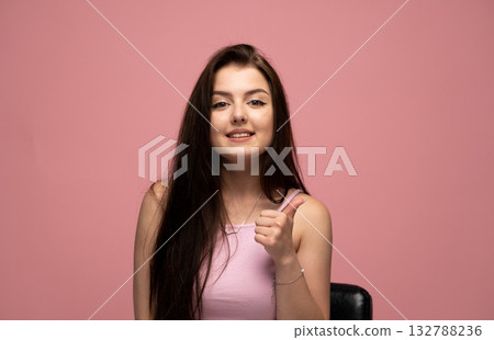 Confident emotion of young woman showing thumbs up in pink top on pink background Confident emotion of young woman showing thumbs up in pink top on pink background 132788236