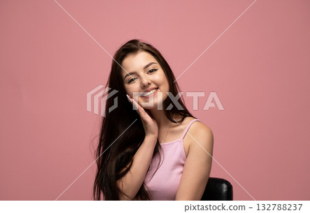 Happy emotion of young woman smiling with hand on face in pink top on pink background Happy emotion of young woman smiling with hand on face in pink top on pink background 132788237