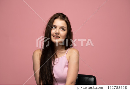 Playful emotion of young woman smiling softly in pink top on pink background Playful emotion of young woman smiling softly in pink top on pink background 132788238