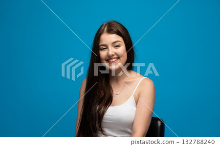 Happy emotion of young woman smiling brightly in white tank top on blue background Happy emotion of young woman smiling brightly in white tank top on blue background 132788240