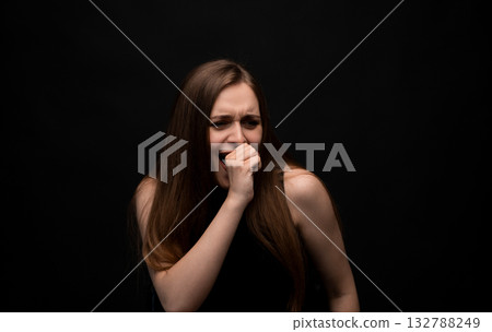 Fearful emotion of young woman covering mouth with hand in black top on dark background Fearful emotion of young woman covering mouth with hand in black top on dark background 132788249