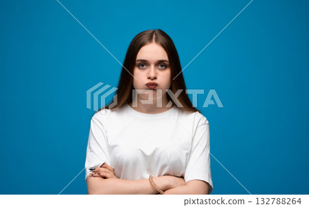 Annoyed emotion of young woman with puffed cheeks in white t-shirt on blue background Annoyed emotion of young woman with puffed cheeks in white t-shirt on blue background 132788264
