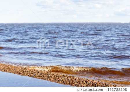 Gentle waves roll onto a sandy shoreline as a calm blue sea Gentle waves roll onto a sandy shoreline as a calm blue sea 132788298