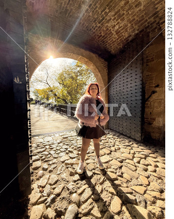 Woman smiling under old arch. Warm light, confidence and enjoyment of autumn city walk. 132788824