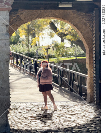 Woman under stone arch on sunny day. Autumn atmosphere, leisure and exploration in historic park environment. 132788825