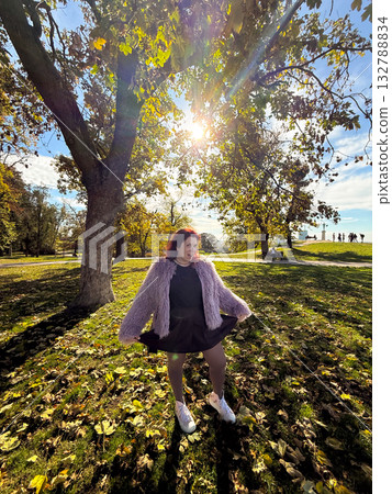 Woman smiling under autumn trees with sunlight. Joy, openness, and self-expression in harmony with nature. Woman smiling under autumn trees with sunlight. Joy, openness, and self-expression in harmony with nature. 132788834