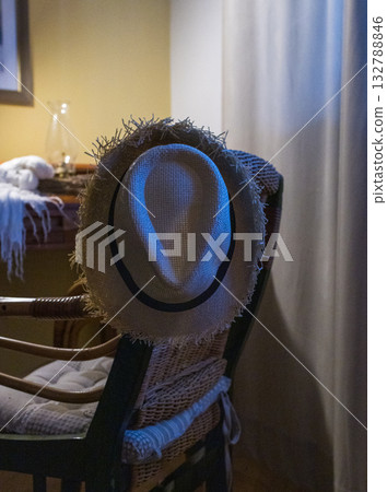 Straw hat hanging on a rattan chair in soft blue light. Vintage workspace. Straw hat hanging on a rattan chair in soft blue light. Vintage workspace. 132788846