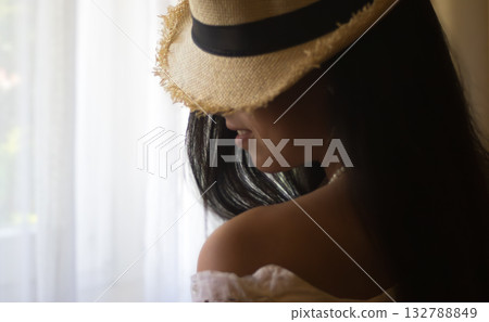 Young hispanic woman wearing straw hat enjoying warm light. Lightes window background. Romantic portrait 132788849