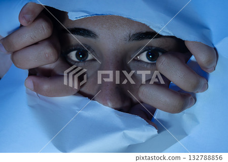 Woman peeking through torn paper with fearful eyes. Concepts of anxiety, hidden feelings Woman peeking through torn paper with fearful eyes. Concepts of anxiety, hidden feelings 132788856